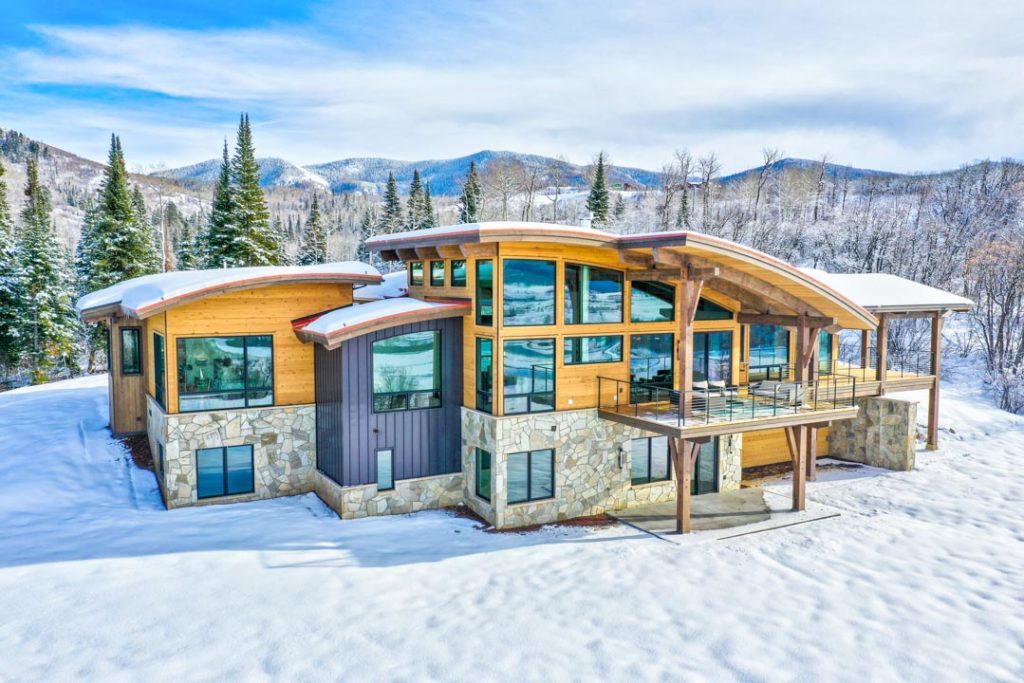 A sizable house featuring a large deck, surrounded by majestic snow-capped mountains.
